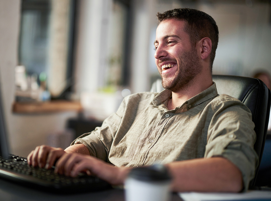 Developer typing on a computer sits in his office and smiles.