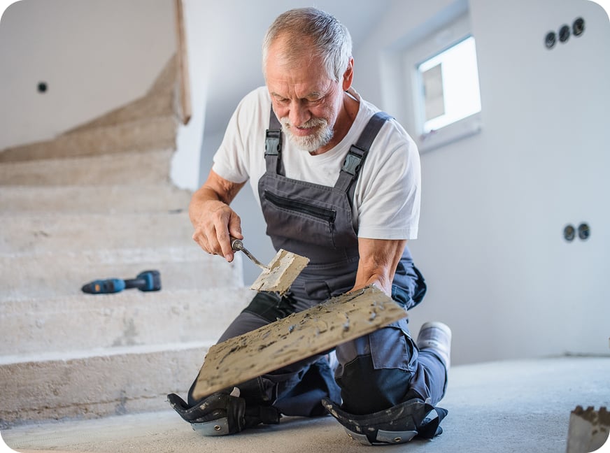 Contractor wearing work overalls prepares to lay tile.